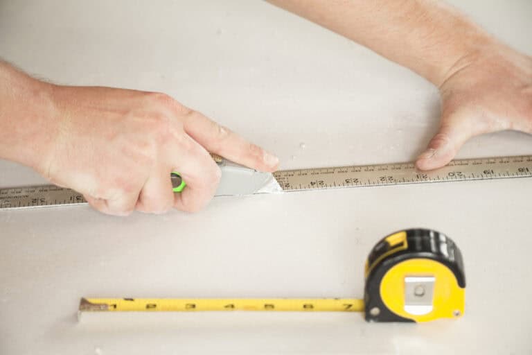 Closeup of male hands measuring and cutting drywall.